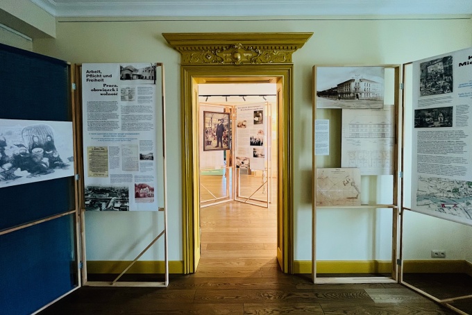 Blick durch einen goldfarbenen Türrahmen in die Ausstellung